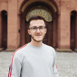 Ein Porträtfoto von Arnold Pernoca. Er trägt kurze, braune Haare, eine schwarze Brille und einen grauen Pullover.
